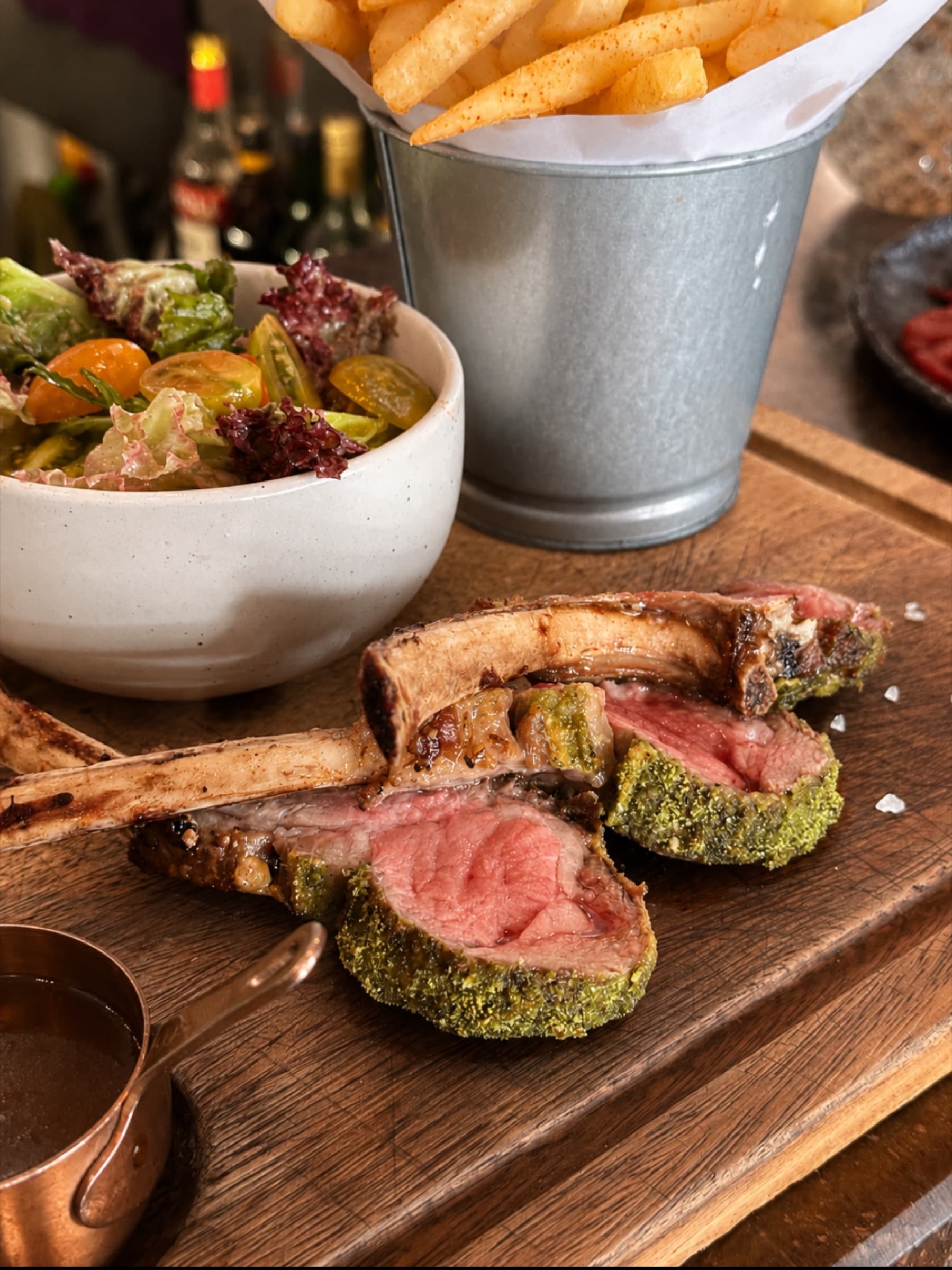 Herb-crusted lamb chops sliced open pink at the center, served with steak fries and a garden salad at Somaha