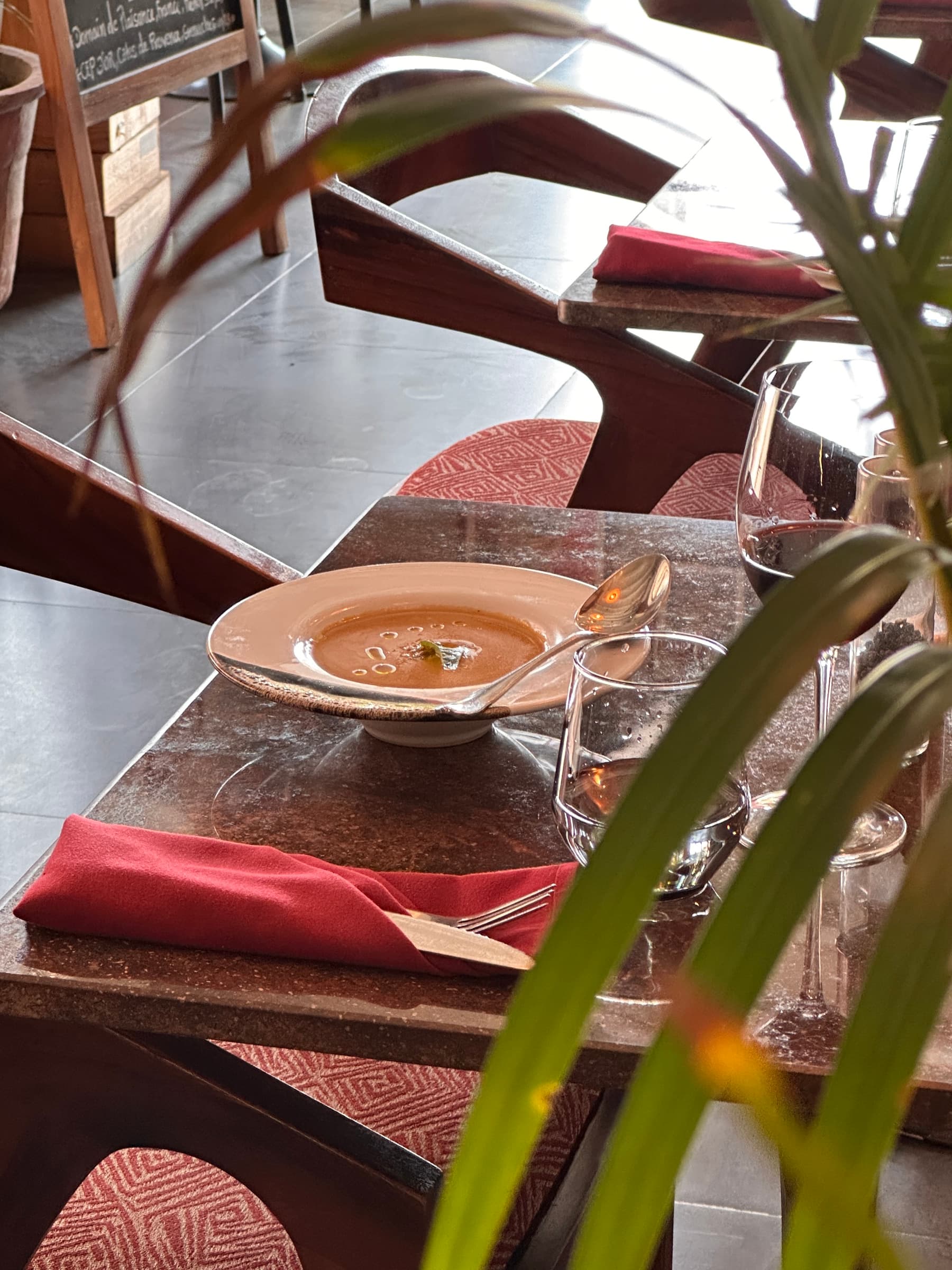 A candlelit table through palm leaves, with a red napkin and wine glasses in Somaha's dining room
