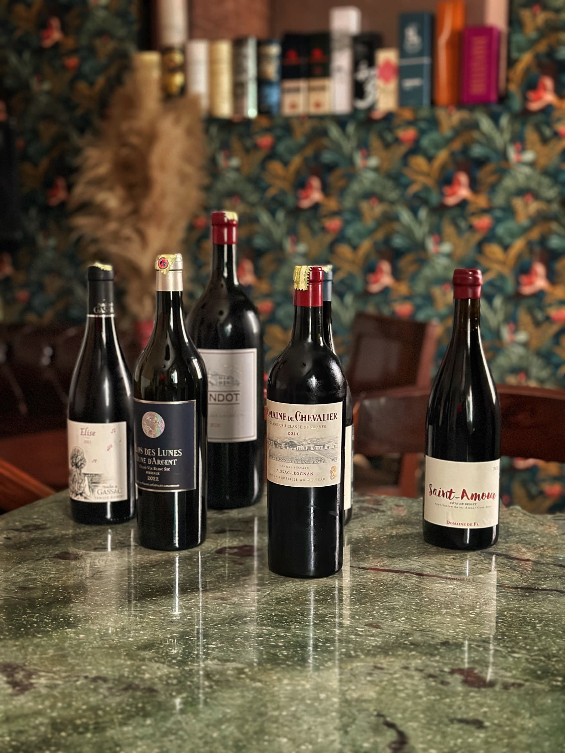 A lineup of wine bottles on a table at Somaha, set against botanical wallpaper