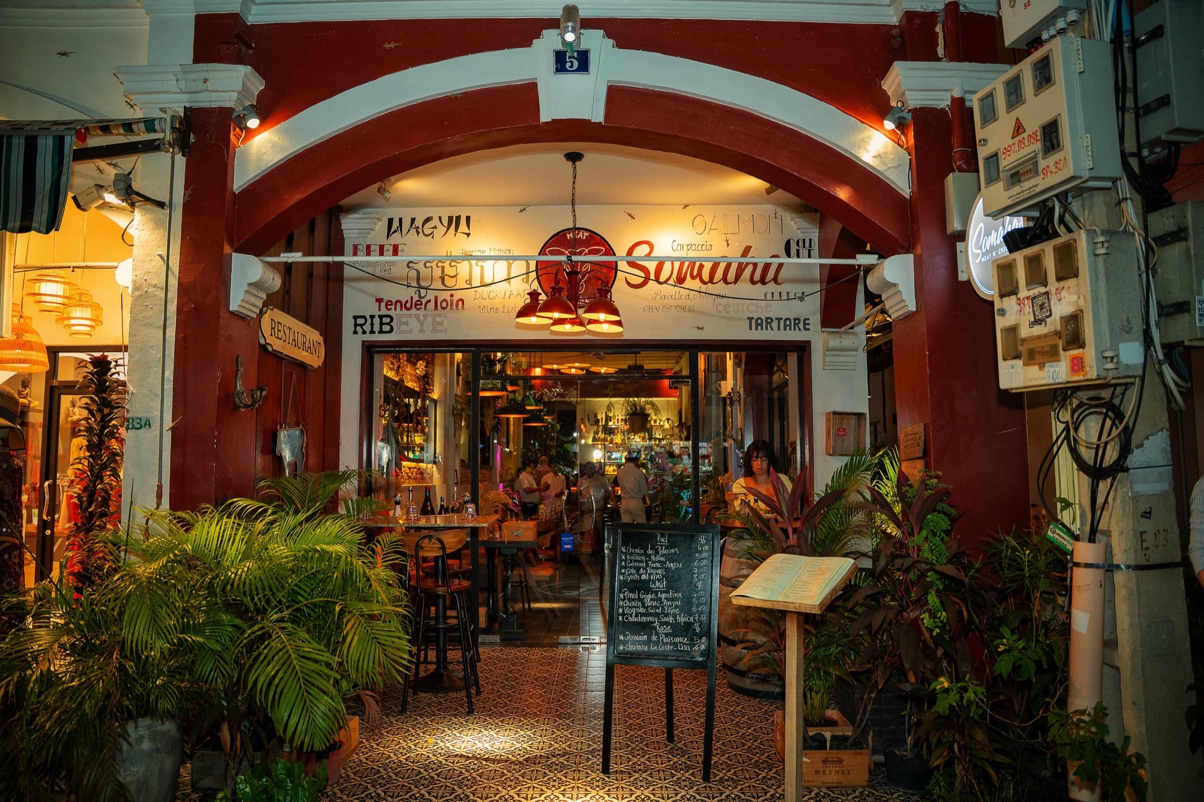 Somaha's entrance archway lit up at night, with the hand-painted Somaha sign and the warmly lit dining room glowing beyond the open doors